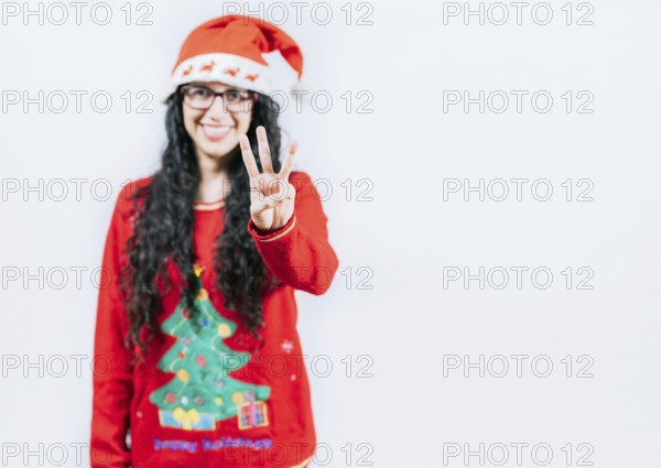 Smiling girl in Christmas sweater counting number 3. Happy girl in Christmas hat counting number