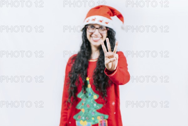 Happy girl in Christmas hat counting number THREE, isolated. Smiling girl in Christmas sweater