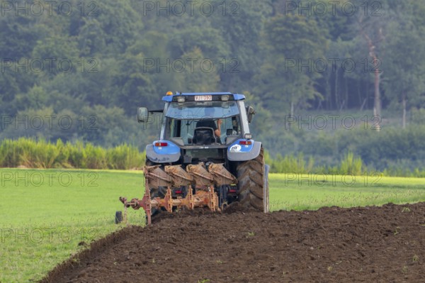 Tractor with plough, agricultural ploughing machine working on a field in autumn, fall in the