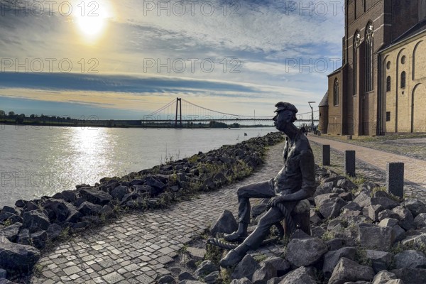 Photo with melancholy mood of bronze sculpture Poortekerl looking at Rhine waiting for ship to