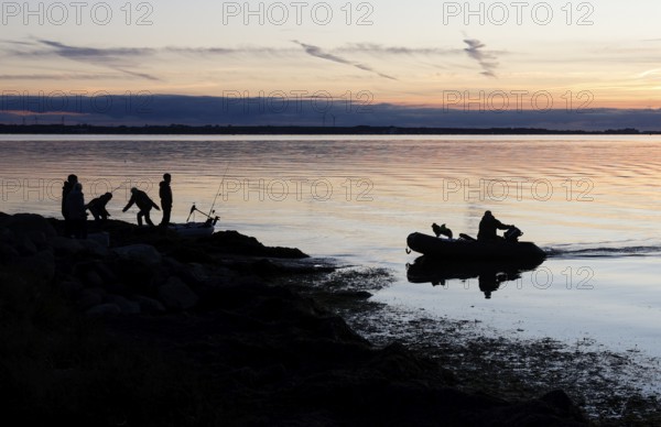 Angler on the beach during sunset, an angler docks on the shore with his inflatable boat and dog,