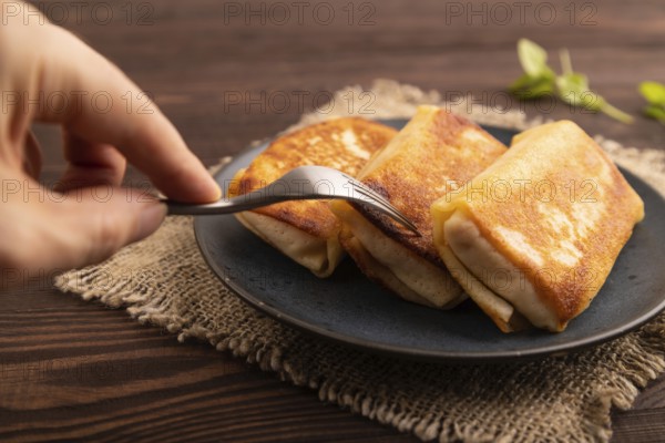 Fried crispy pancakes with meat and cheese with hand on brown wooden background and linen textile.