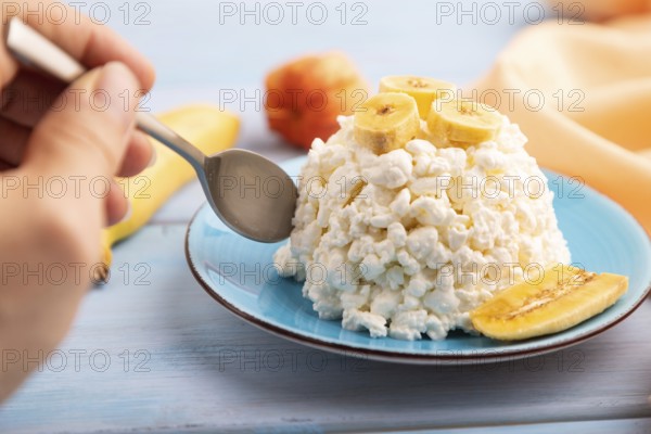 White ?ottage cheese, Curd, with Banana with hand on blue wooden background and orange textile,