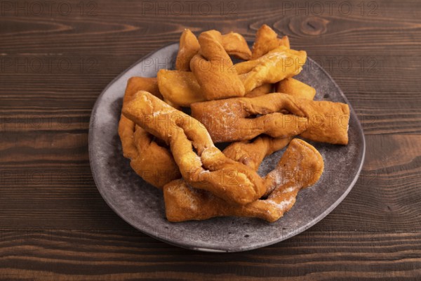 Crunchy biscuit Brushwood cookies sprinkled with powdered sugar on brown wooden background, side
