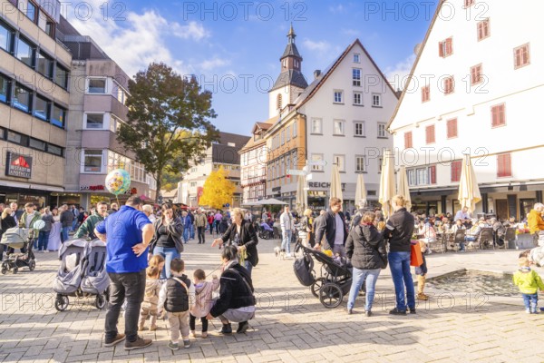 Bustling market square with families, church in the background, sunny day and historic houses,