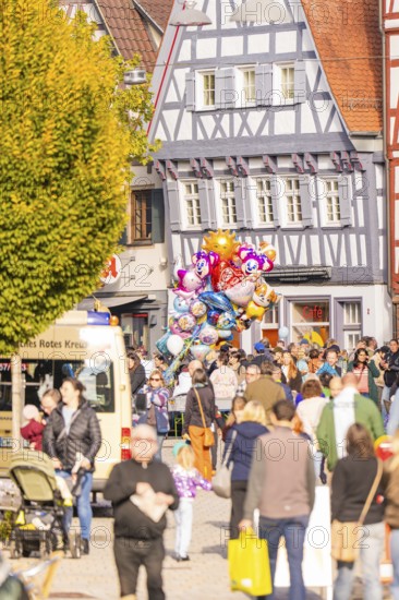 People pass half-timbered houses, colorful balloons over a lively crowd of roads, Urschelherbst