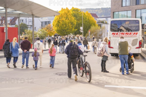 Busy scene at a bus stop, people on the move, a cyclist pushes his bike, Urschelherbst street