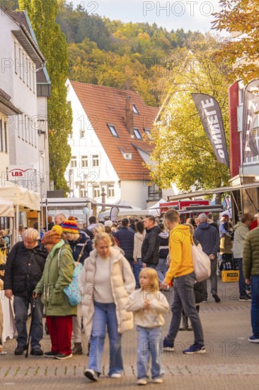 Families stroll across a busy market street under autumn leaves, Urschelherbst street festival,