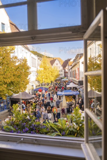 From a window you can see a lively street full of people and colorful market stalls under yellow