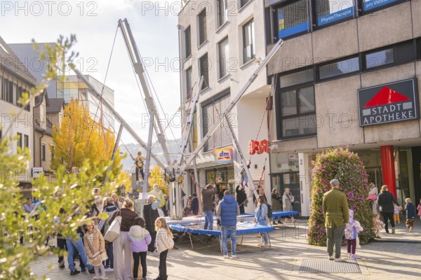 People enjoy activities on bungee trampolines in front of municipal shops and a pharmacy,