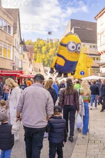 A minion balloon hovers over a family strolling through the city in sunny autumn, Urschelherbst