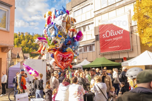 Colourful balloons over a crowd of people on a sunny market square surrounded by buildings,