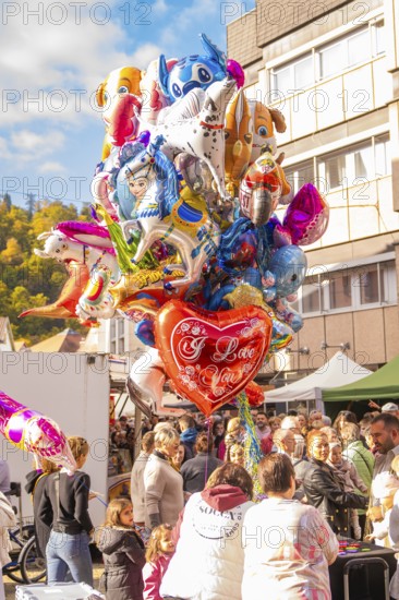 Various colorful balloons, including a heart with 'I Love You, 'float above a celebratory crowd,