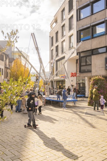 A group of people gather around bungee trampolines in an urban area, Urschelherbst Street Festival,
