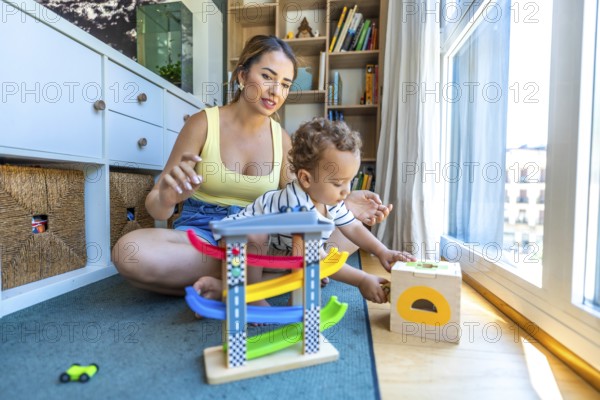 Young mother watching her baby son playing with a toy car garage and a shape sorter on the floor at