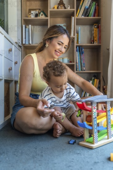 Happy mother and son playing with toy cars and garage, sitting on the floor in the playroom, having