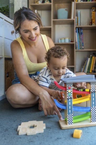 Mother and baby son sitting on the floor, joyfully playing together with a colorful toy car and
