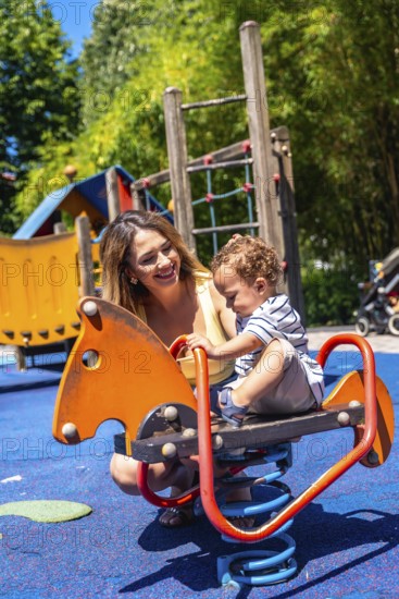 Smiling mother spending time with her baby son, enjoying a sunny day at the playground, promoting