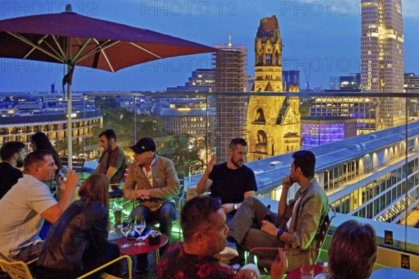 People on an outdoor terrace in the evening with a view of the illuminated Kaiser Wilhelm Memorial