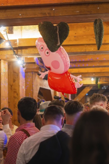 A pink heart-shaped balloon floats above a crowd in a traditional wooden house, Cannstatter Wasen
