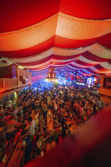 Lively celebration in a decorated beer tent with red and white stripes and lots of people,