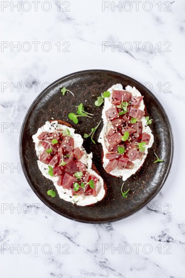 Sandwiches, rye bread with cream cheese, sliced tuna fillet with herbs, breakfast on a black plate,