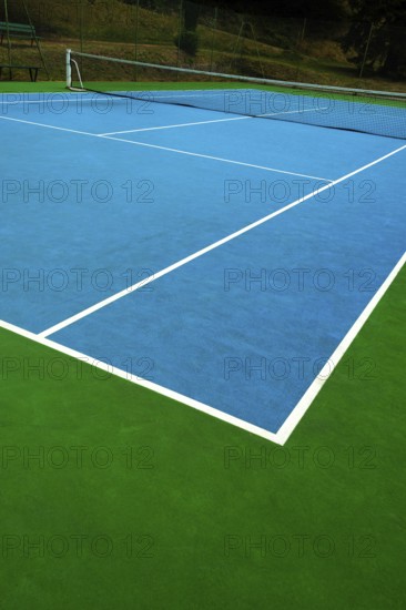A vibrant tennis court with a blue surface contrasts against the green edges. The bright white