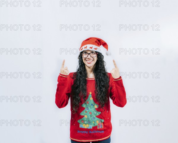 Smiling girl in Christmas hat pointing up isolated. Beautiful girl in Christmas sweater showing and