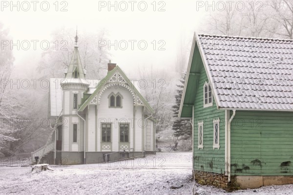 Old idyllic white wooden house with carpentry and a green garden shed on a cold winter day with