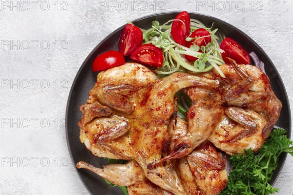 Baked quail, served on a plate with crispy lettuce leaves, fresh tomatoes and herbs, on a dark