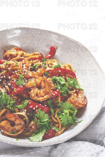Udon noodles, shrimp with vegetables and fresh herbs, in a bowl with chopsticks, light background,