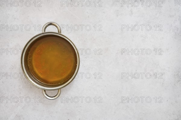 A silver pot filled with rich, golden mushroom broth on a smooth light gray surface. The broth