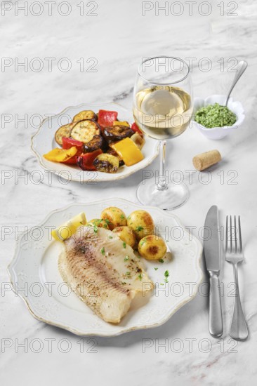 A beautifully arranged dinner includes a plate with a tender fish fillet, roasted potatoes, and