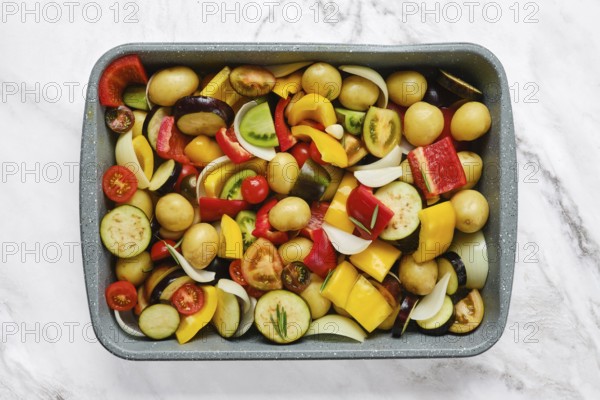 A vibrant mix of fresh vegetables is arranged in a baking tray, showcasing colorful peppers,