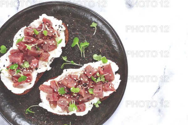 Sandwiches, rye bread with cream cheese, sliced tuna fillet with herbs, breakfast on a black plate,