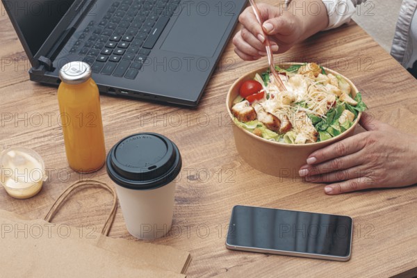 A woman is working on a laptop at home, there is food on the table, salad, coffee and juice,