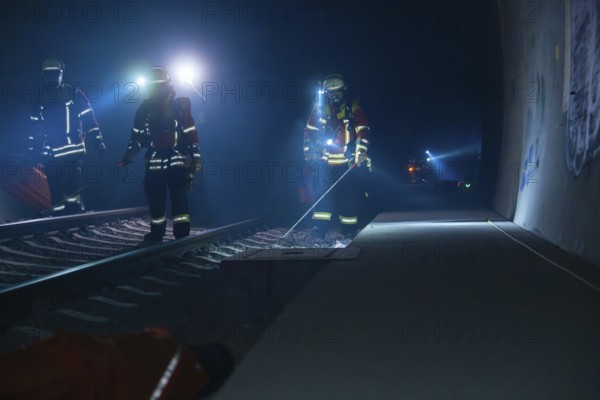 Three firefighters walking along a tunnel wall, torch lit, fire drill in the new tunnel of the
