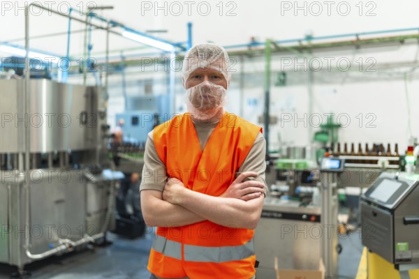 Worker standing proudly with crossed arms, wearing a safety vest and hairnet in a clean, automated
