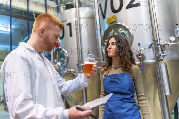 Brewery workers evaluating beer sample for quality control, holding clipboard and glass in brewing