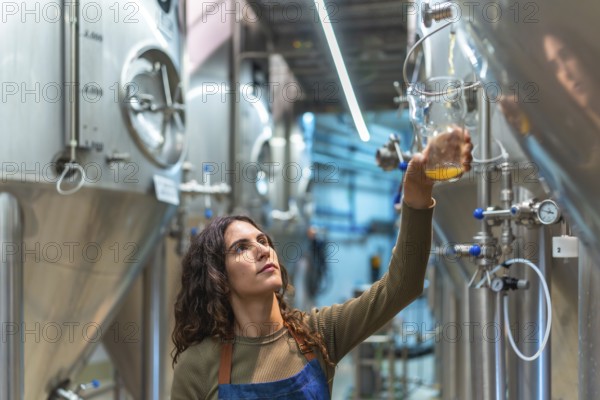 Woman brewer performing quality control, holding a glass sample of fresh beer, standing in a modern