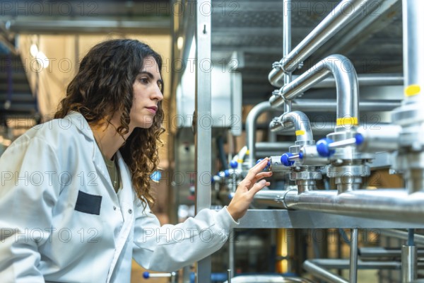 Young woman engineer wearing a lab coat and safety glasses. Meticulously adjusting valves on