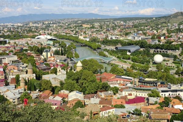 Cityscape of Tbilisi with lush greenery and diverse architecture during a sunny days under a clear