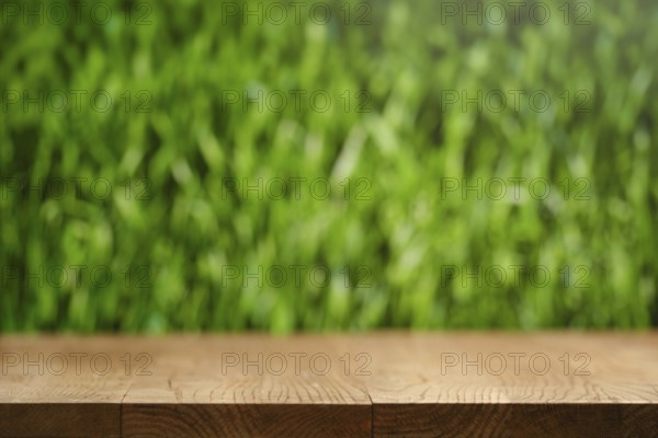 A simple wooden table stands in front of a softly blurred lush green grass background. The scene