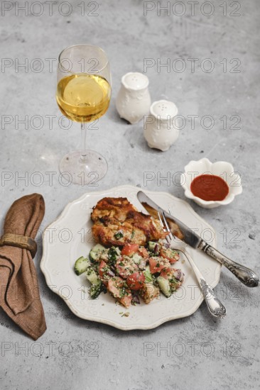 A beautifully arranged meal includes a golden glass of wine, a serving of baked meat, fresh salad