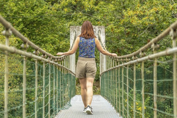 Female tourist enjoying a peaceful walk across a metallic hanging bridge, surrounded by lush green
