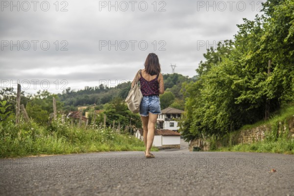 Young woman tourist walking on a road approaching benia de onis village in asturias, spain, during