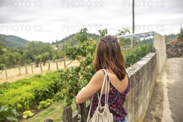Young woman tourist with backpack is enjoying the view of a peach orchard and a vegetable garden in
