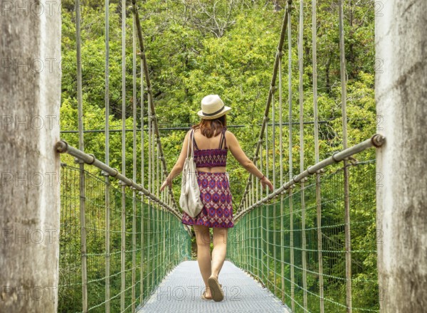 Young woman tourist with a hat and bag walking on a hanging bridge over the dobra river, enjoying a