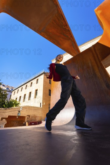 Woman performing a dynamic dance move, expressing freedom and urban culture against a vibrant blue