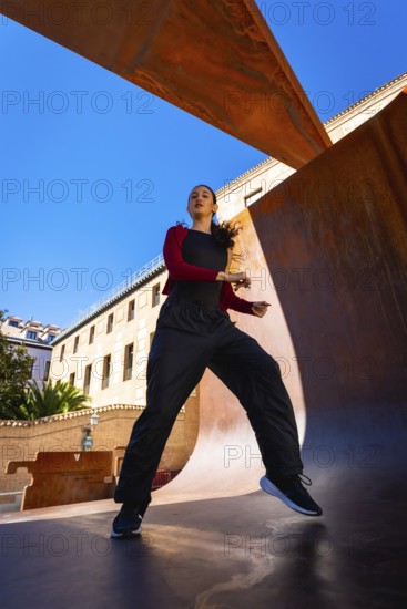 Young woman moving energetically, practicing dance in an urban setting, with modern corten steel
